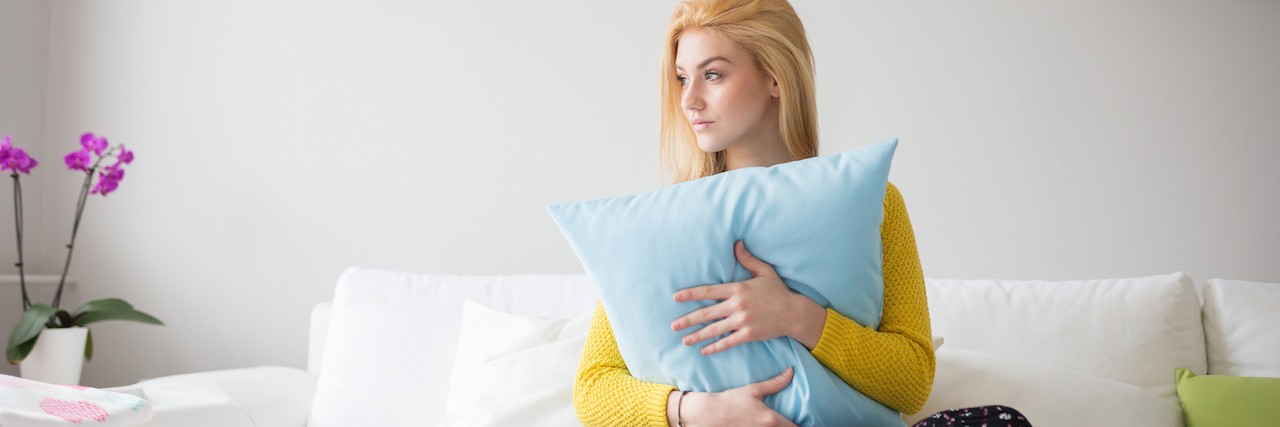 When You Miss Your Eating Disorder in Recovery A young woman holds her pillow as she sitts on a bed
