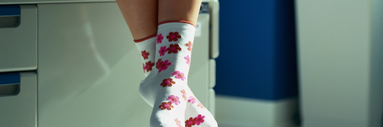Close up of a woman's feet hanging over a hospital bed in her hospital gown and socks.