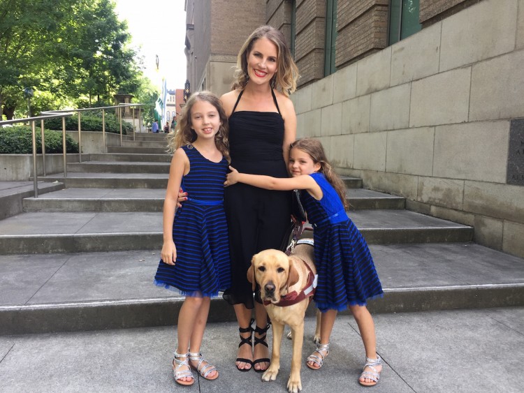 woman and two girls stand on steps with guide dog