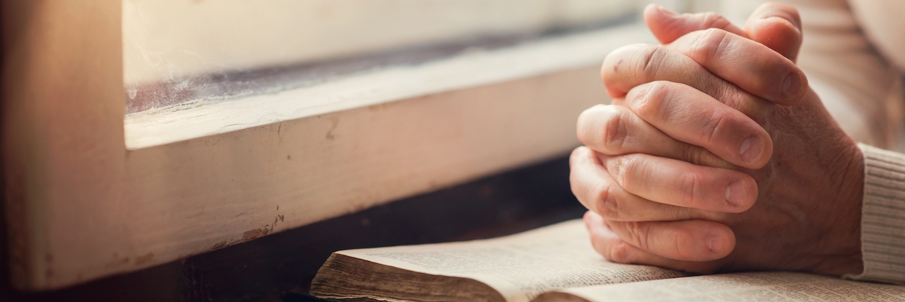 Hands of woman folded in prayer on top of Bible