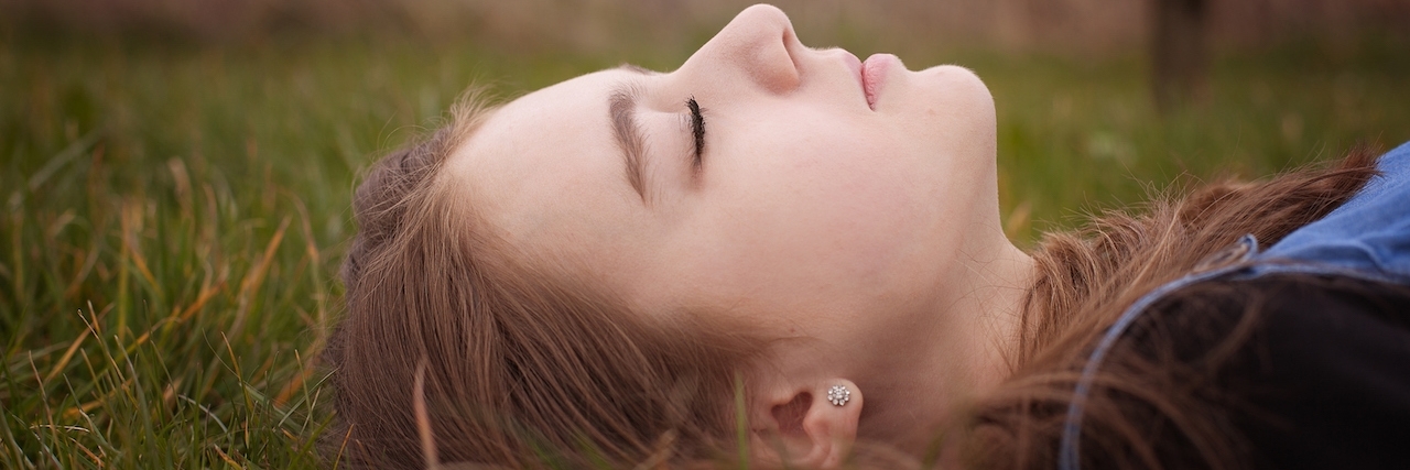 Up close, side shot of a young girl laying in the grass with her eyes closed