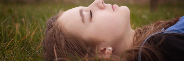Up close, side shot of a young girl laying in the grass with her eyes closed