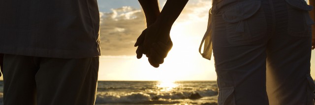 Couple holding hands with beach in the background