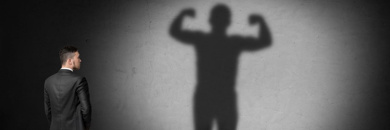 Why I Choose to Celebrate My Bipolar Diagnosis Man stares at a shadow of himself with muscles on the wall