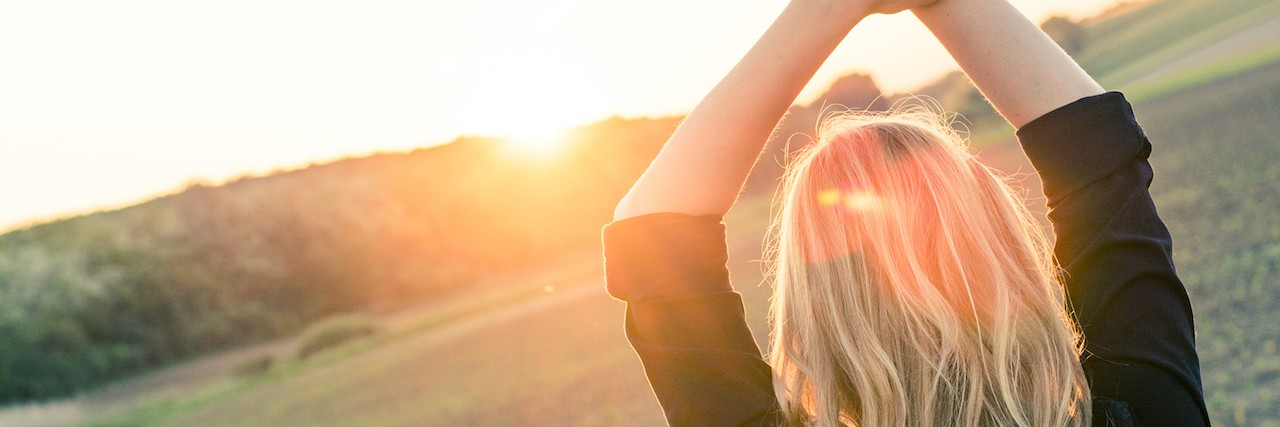 Living With Anxiety: Being Both Broken and Strong Woman raising her arms in the air with the sunset in the background