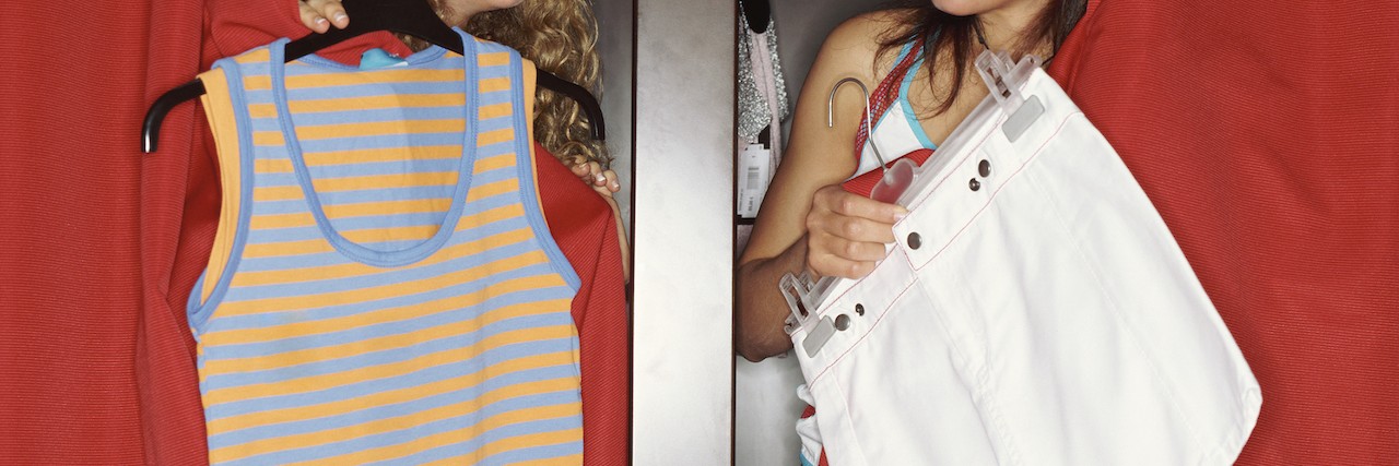 Two girls poke their heads out of their dressing rooms to show each other clothes