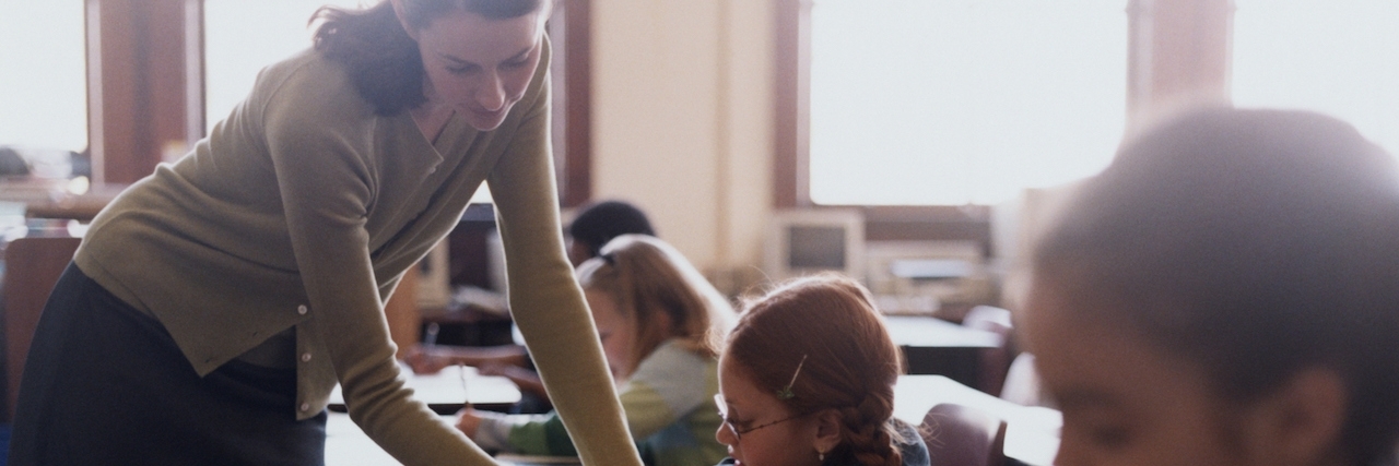 To the Teacher Who Stood Up to Me When I Was Bullied Teacher leans over student's desk, helping with assignment