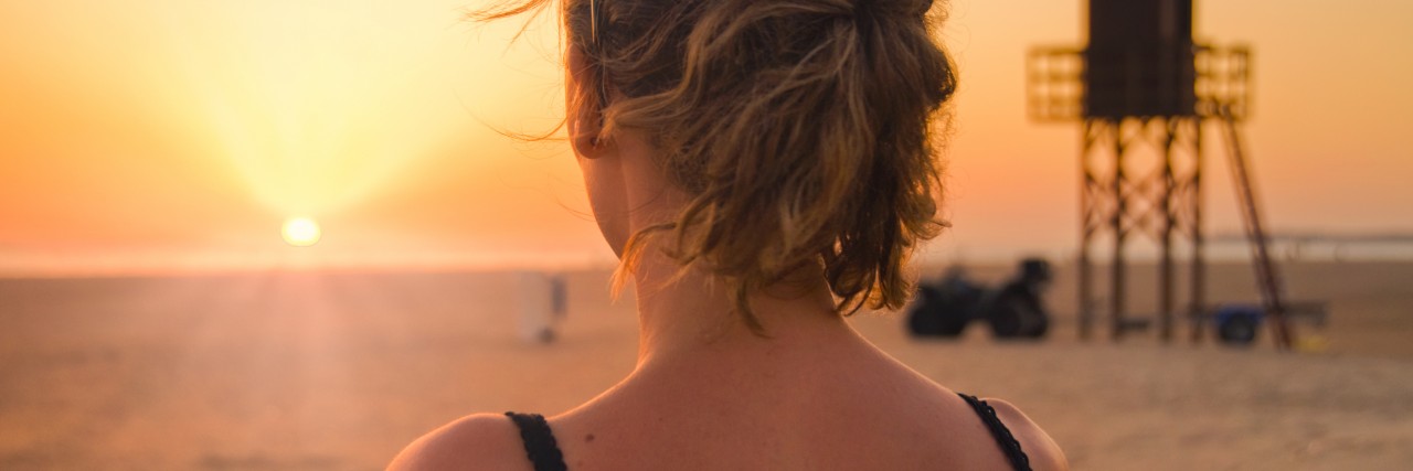 woman standing on the beach gazing out at the ocean in contemplation