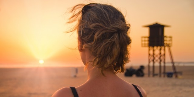 woman standing on the beach gazing out at the ocean in contemplation