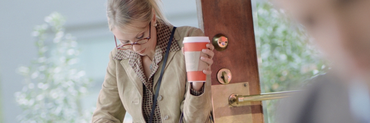 Parkinson's Disease Symptoms That Most Impact My Everyday Life Businesswoman with to go coffee looking in purse at cafe.