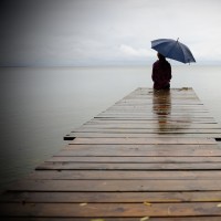 A man holdning an umbrella, sitting at the end of a dock