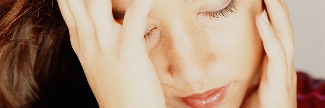 The Exhaustion of Living With Mental Illness Young woman with eyes closed, head in hands,