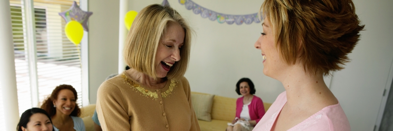 Why Health Isn't Everything When Parenting a Child With a Rare Disease Mature woman feeling pregnant woman's bump at baby shower, laughing