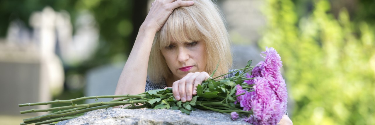 Woman mourns with her hand on headstone in cemetery in closeup