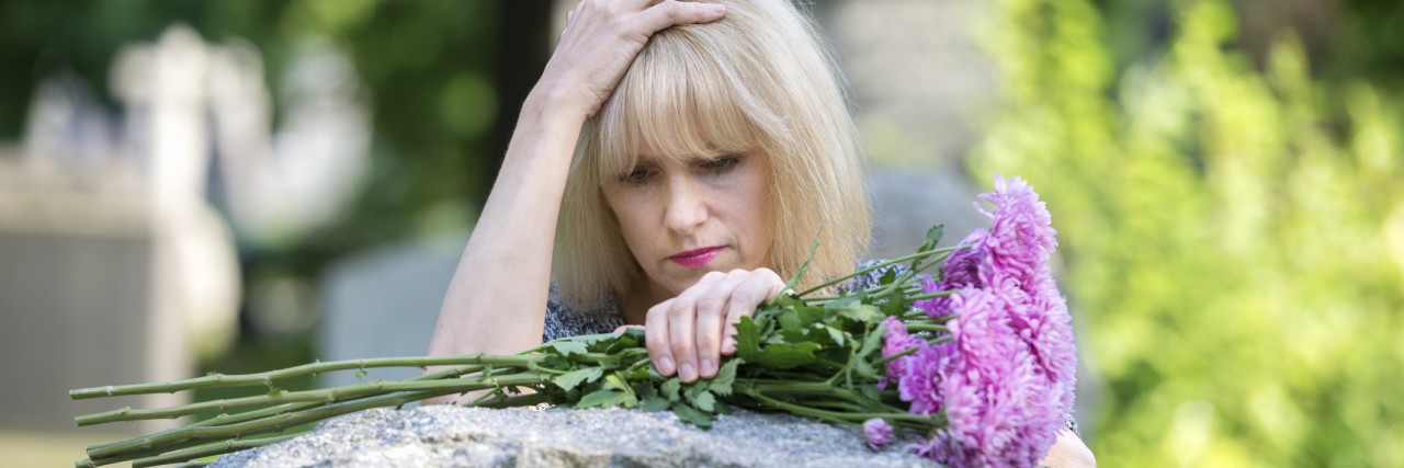 Answering the 'Why?' After a Child's Death Woman mourns with her hand on headstone in cemetery in closeup