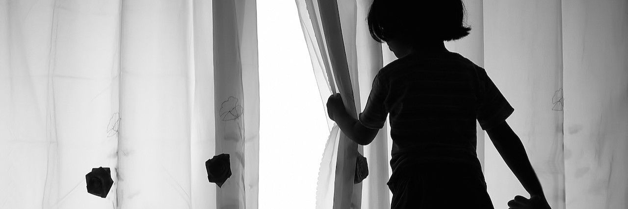 girl holing a doll, looking out the window