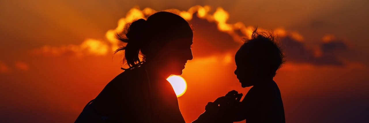 mom holding her son's hands in the sunset