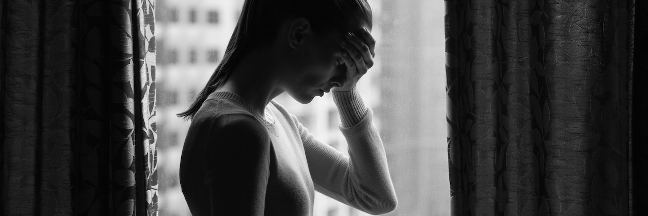 Feeling Like You Don't Have the Right to Be Upset About Chronic Pain woman standing in front of window with hand on head