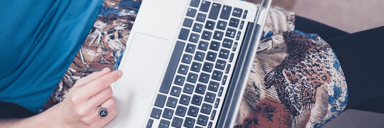 A young woman is sitting on a sofa at home in her living room and is using a laptop computer