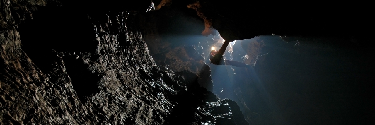 Feeling Stuck and Dark in the Pit of Depression Caver, spelunker abseiling in a deep pothole