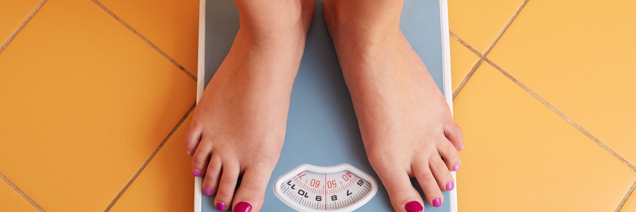 Body Image and Trying to Lose Weight After Lyme Disease Diagnosis A pair of female feet standing on a bathroom scale