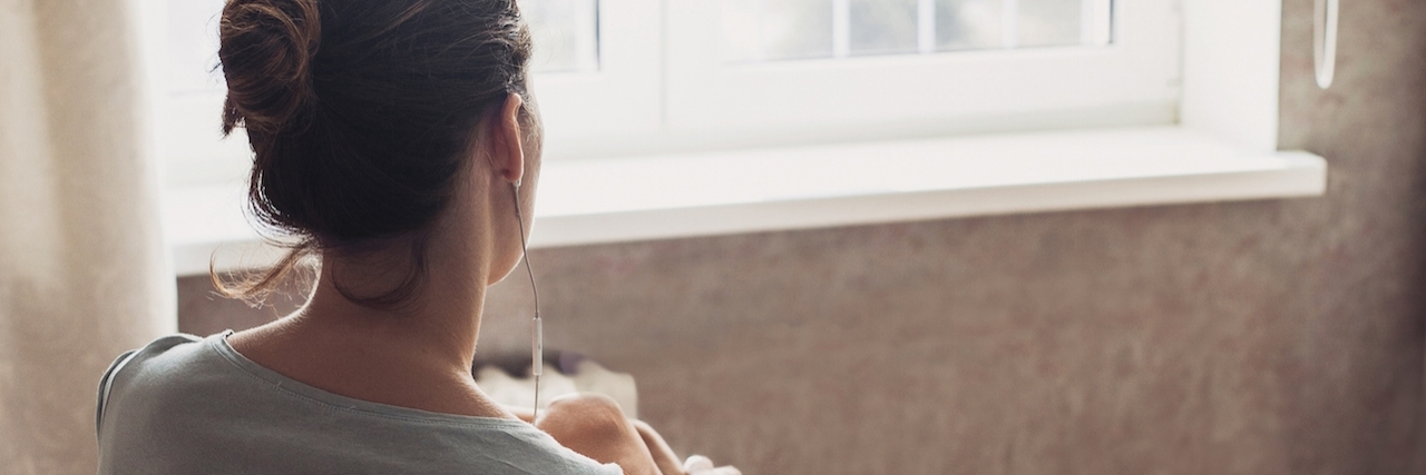Staying Home and Resting for Your Mental Health Woman sitting on bed, staring out window, next to a cup of coffee