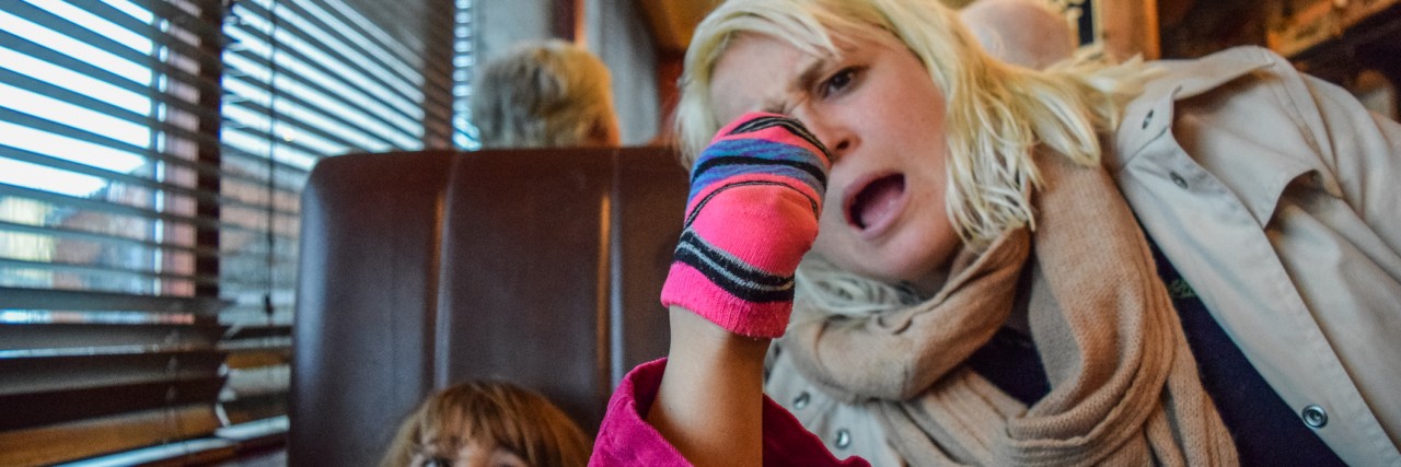 Little girl puts her socked foot on the table at a restaurant, her mother looks on