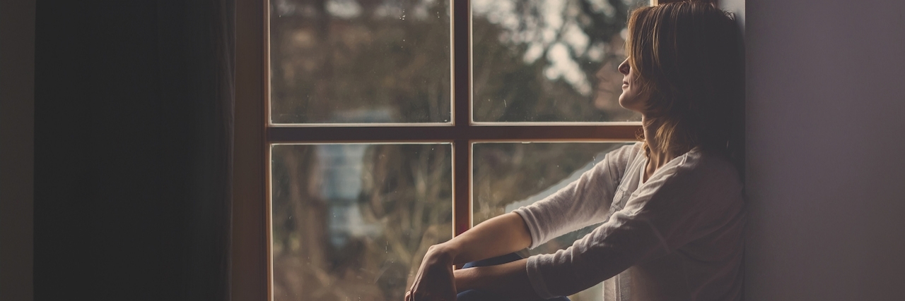 Self-Care Ideas During Difficult Times Woman sitting on a windowsill, looking outside