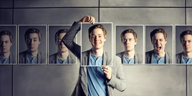 Guy holding a photo in front of his face of him looking happy, surrounded by photos of him looking sad