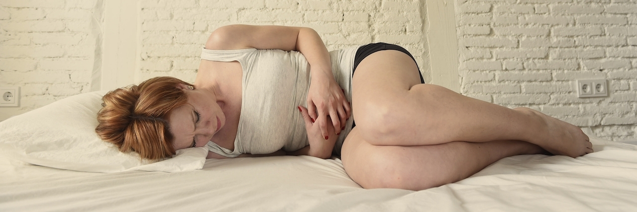 How to Deal With Fibromyalgia on Your Period young woman in stomach belly period pain suffering in bed