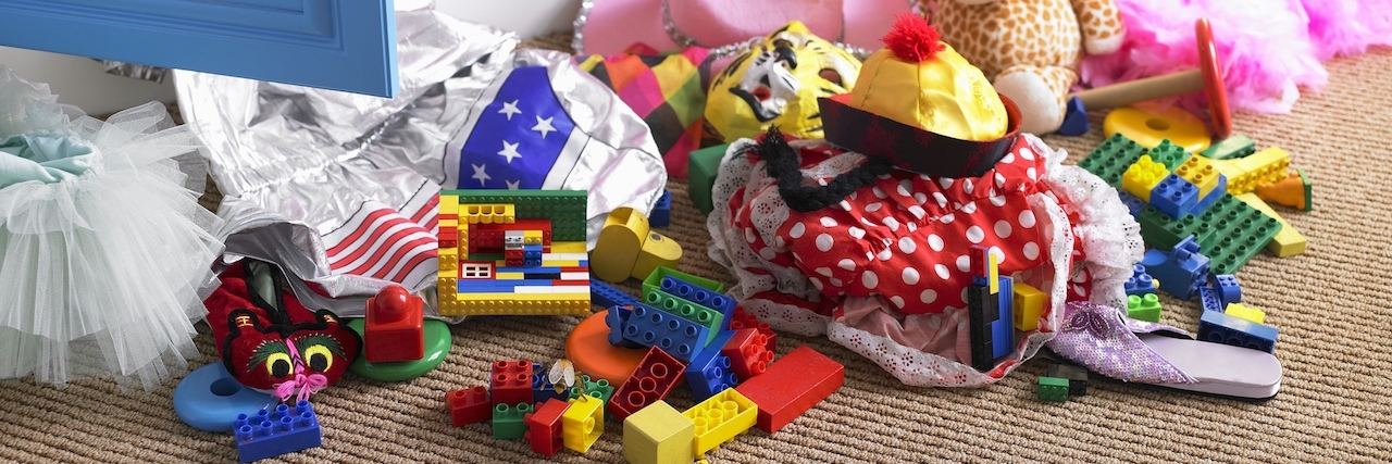 Children's toys and items of clothing strewn on floor near open cupboard door in bedroom