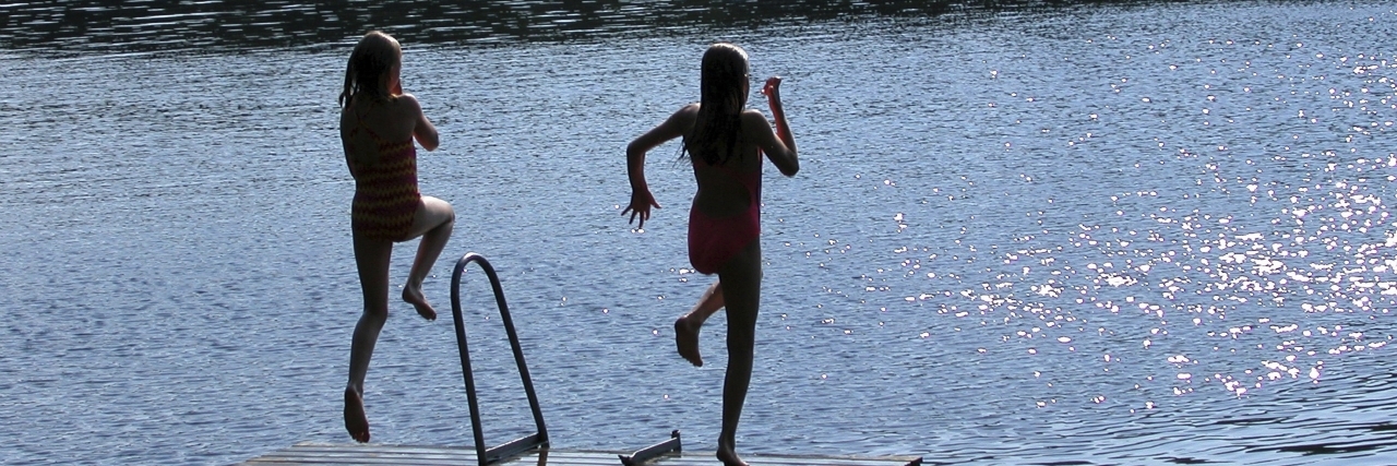 Girls jumping from pier into lake.