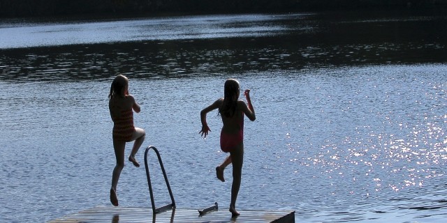 Girls jumping from pier into lake.