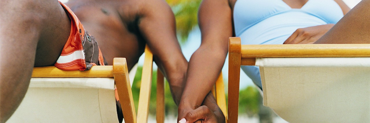 Couple Sitting on Deck Chairs, Holding Hands on the Beach