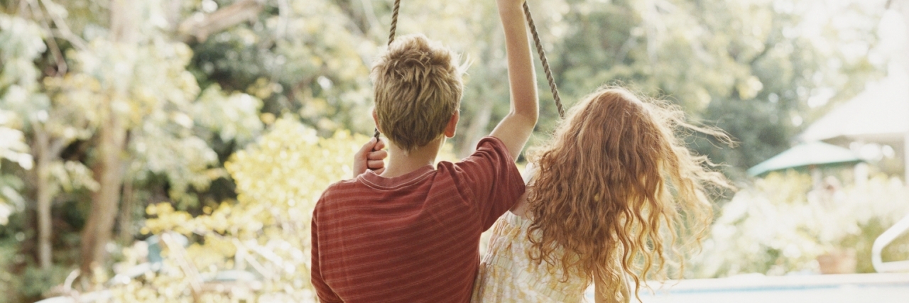 Rear View of a Boy and a Girl Sitting Side by Side on a Swing