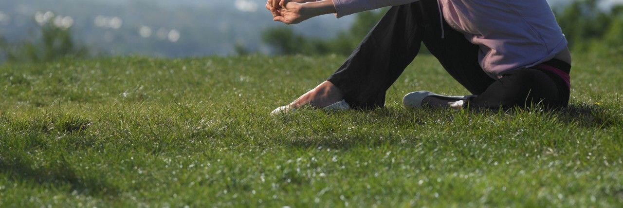 Self-Care Suggestions When Living With Myotonic Dystrophy Young woman sitting on grass in sport clothes, cityscape in background