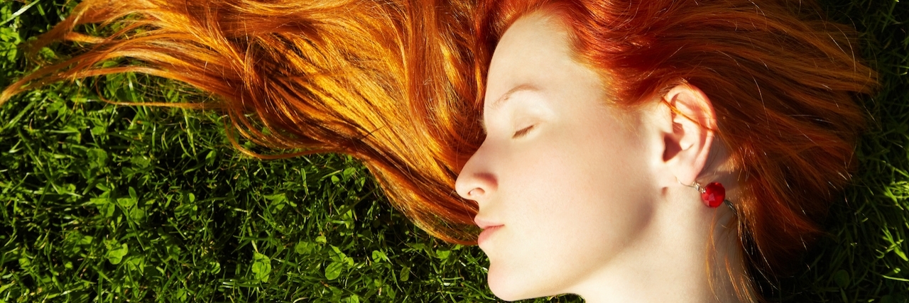 Up close shot of woman with red hair lying on the grass