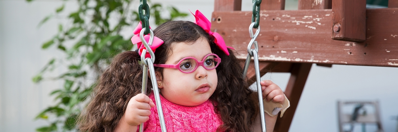 Madison in a swing wearing glasses, a little girl with a rare disease