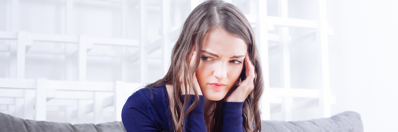 Explaining Anxiety and Depression to a Loved One Woman sits on couch holding her temples