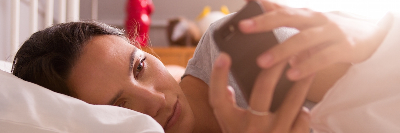 Advice for Spending Energy With Fibromyalgia or Chronic Fatigue Woman Lying In Bed Checking Messages On Mobile Phone