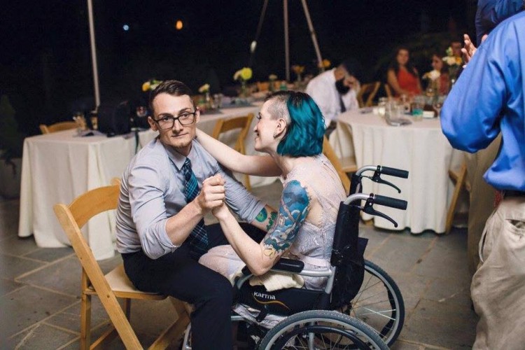 woman in wheelchair dancing with husband sitting in chair