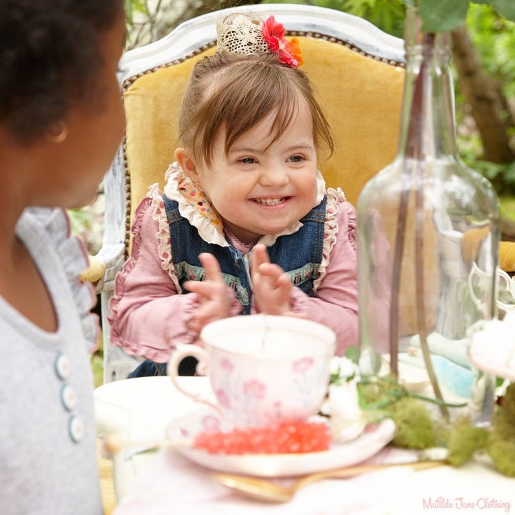 Young girl sitting at table, modeling for Matilda Jane Clothing