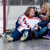 A mom and her two daughter sit on a hockey rink, smiling and laughing