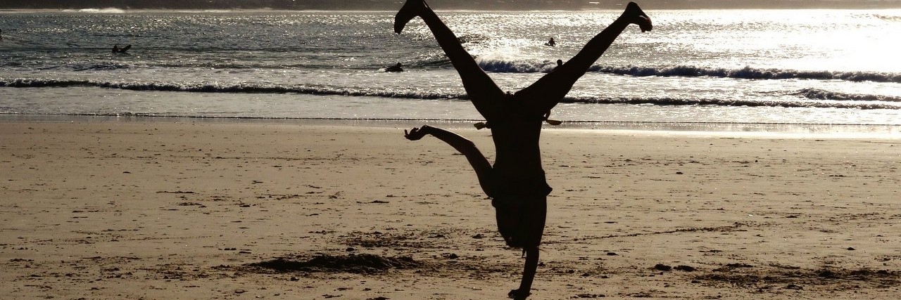 Person doing a cartwheel on the beach with the sun setting in the background