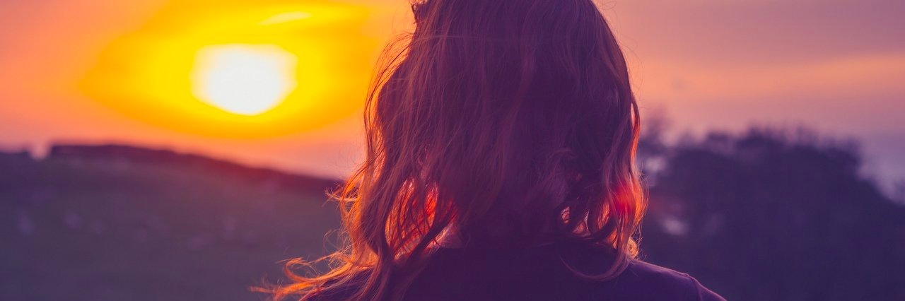 Young woman admiring the sunset over fields