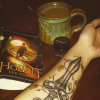 Woman shows her sword tattoo on her forearm, with book and coffee next to her