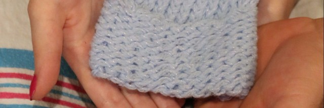 three sets of hands hold a tiny blue knit hat