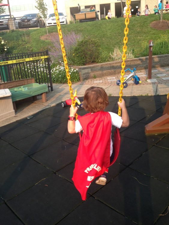 Cohen on a swing, wearing his superhero cape.