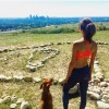 Woman overlooking a city skyline from a hill with her dog next to her