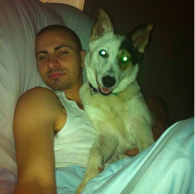 A young man holding his dog against his chest as he lies in bed.